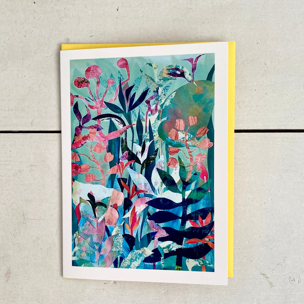 A botanical art print with a colorful abstract leaf pattern in shades of teal, pink, and navy, displayed on a light gray wood background with a yellow cardstock backing visible.