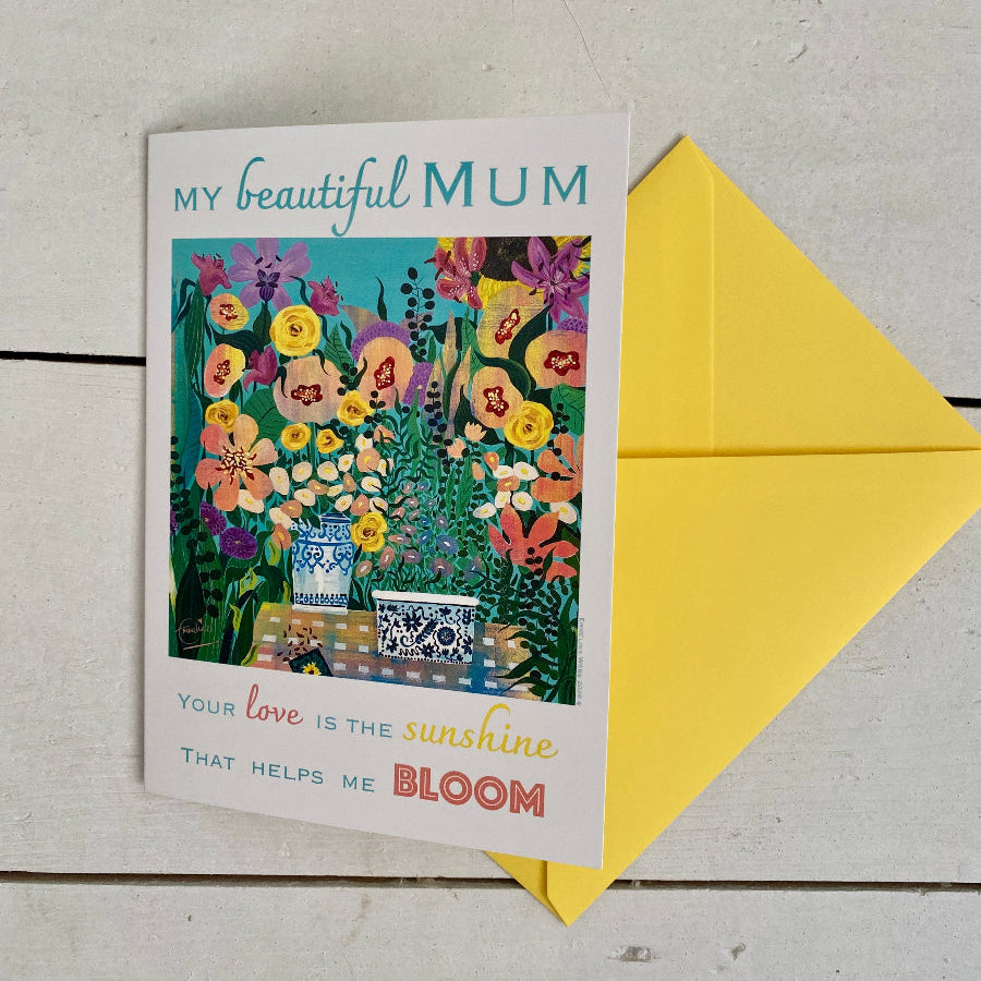 A floral greeting card addressed to 'My beautiful mum' with a bright yellow envelope, placed on a light wood surface.