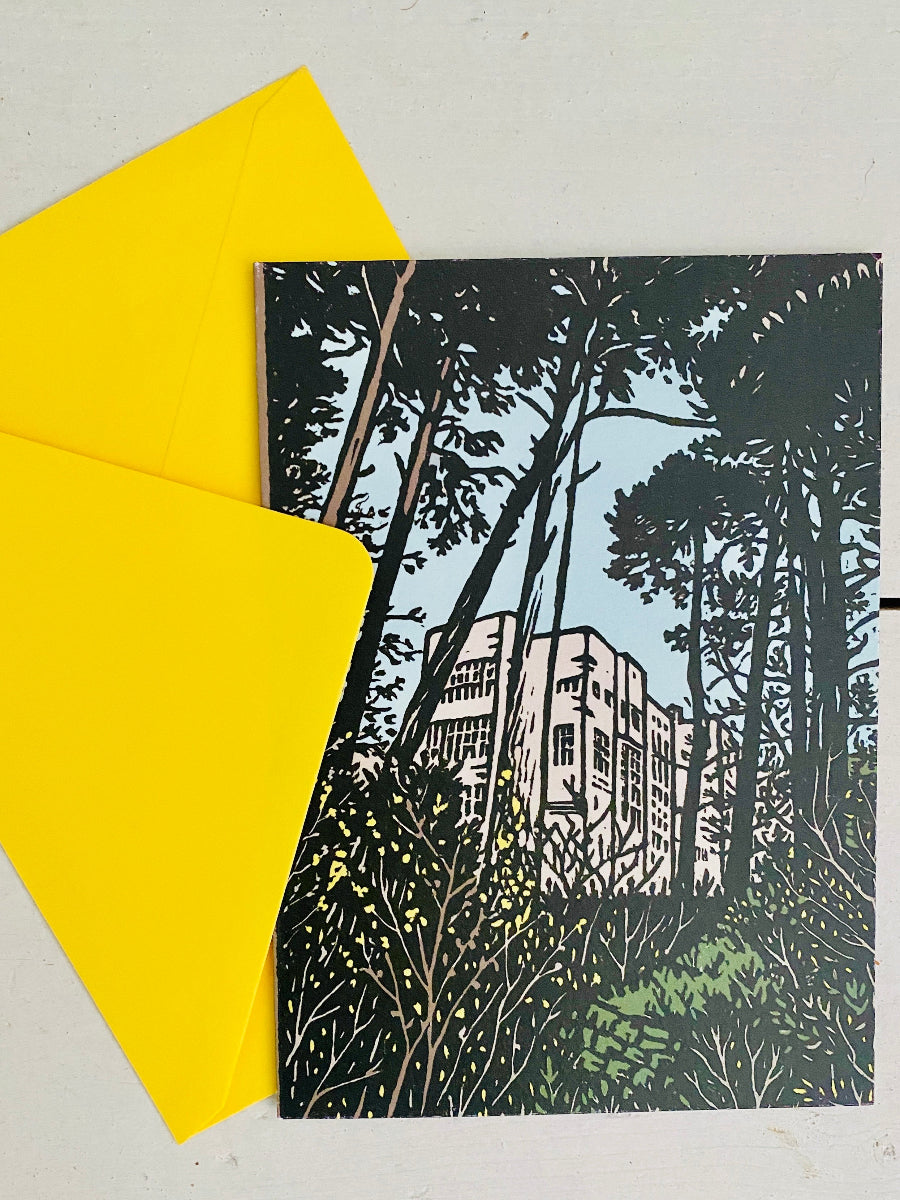 A square art print or card featuring a black-and-white architectural illustration of a building surrounded by tall trees and greenery, placed on a light surface with a bright yellow envelope behind it.