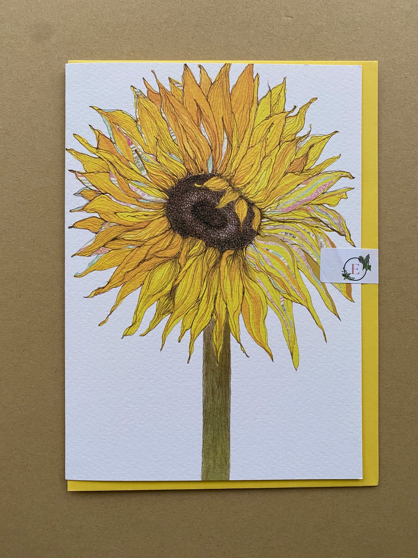 A square art print card featuring a detailed illustration of a yellow sunflower, set against a white background with a yellow envelope displayed on a textured brown surface. With a paper clasp sticker.