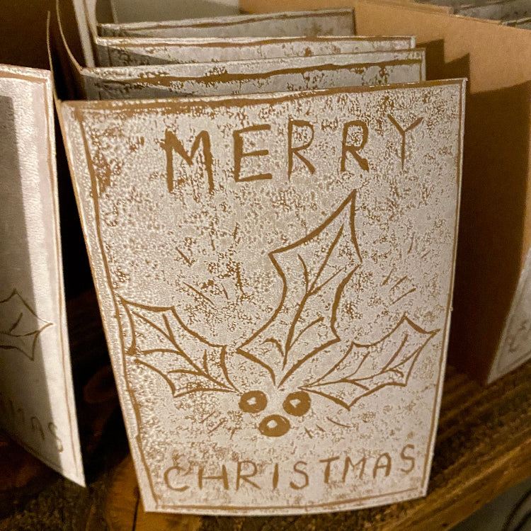 Vintage-style 'Merry Christmas' card with holly design on a wooden surface.