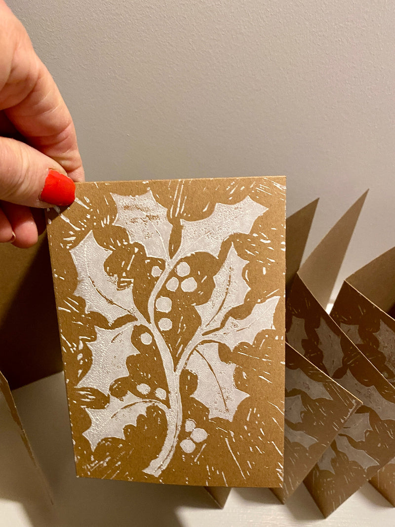 Hand holding a lino printed card with a floral holly design on a plain background