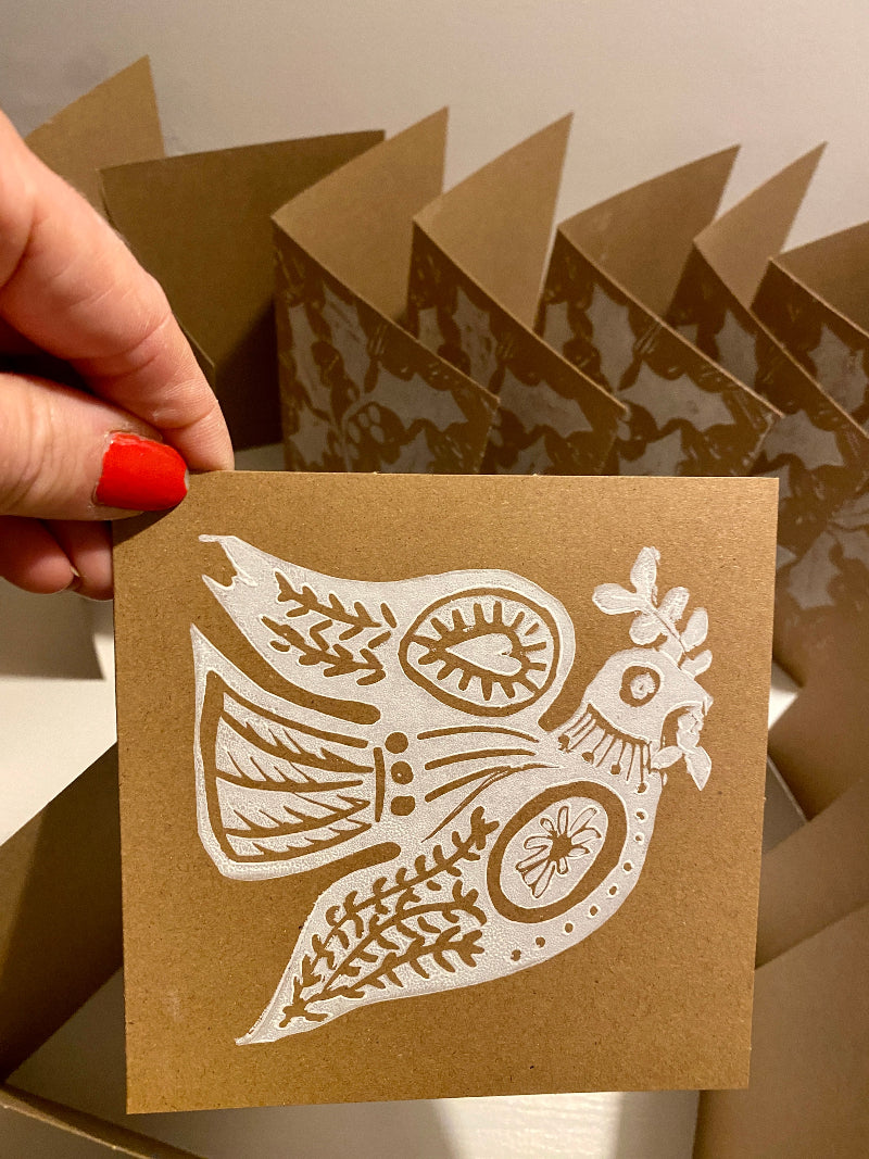Brown paper lino printed card with white cut-out design of a dove held by a hand.