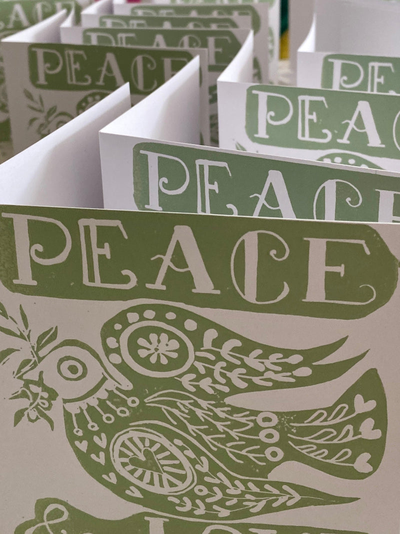 Stack of hand printed Christmas greeting cards with 'PEACE' text and dove design in green and white