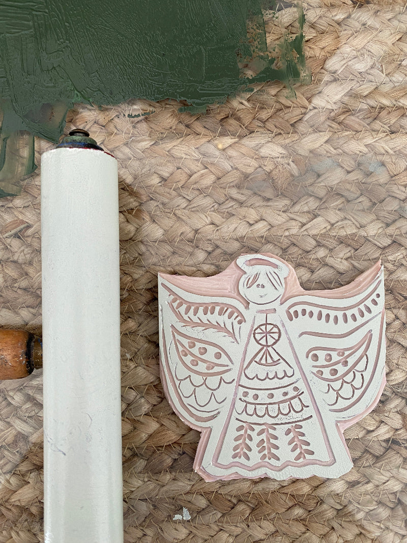 Decorative wooden lino stamp with intricate angle design on a woven surface and printmakers roller