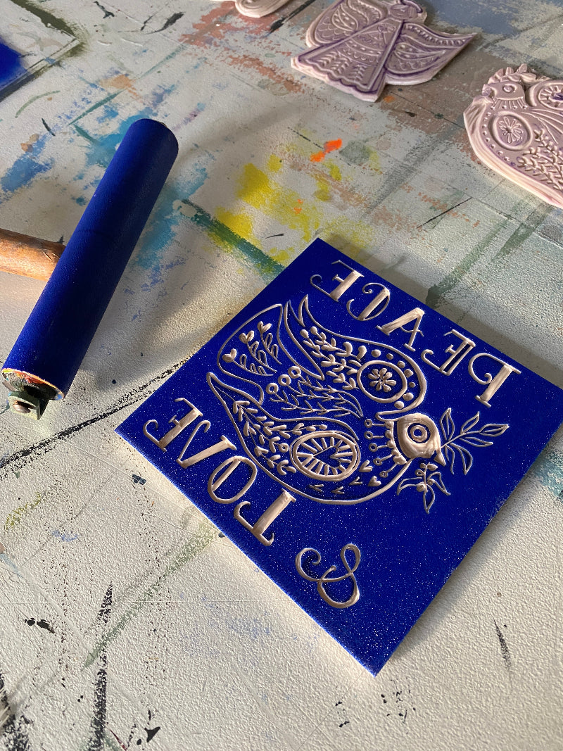 Decorative blue stamp with intricate design on a textured surface and lino printing blocks and roller