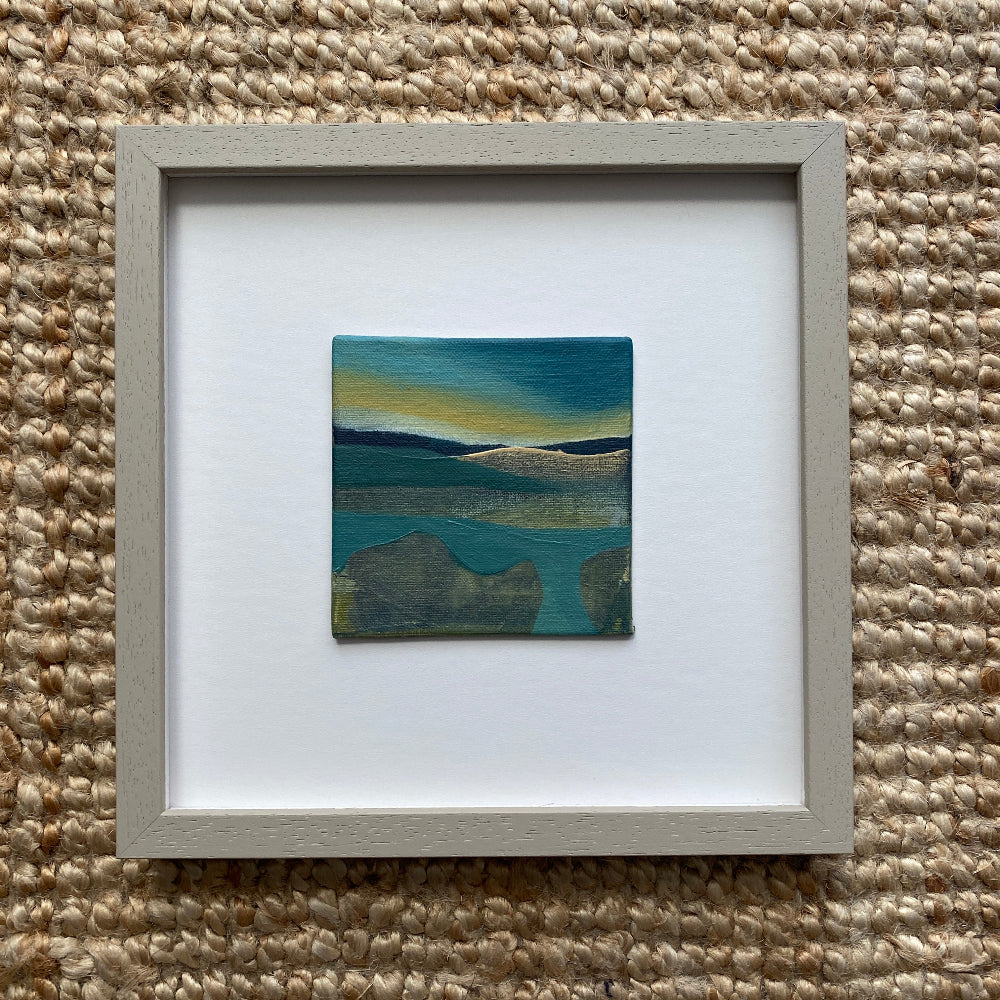 Framed artwork of a landscape with blue and green hues on a textured beige surface.