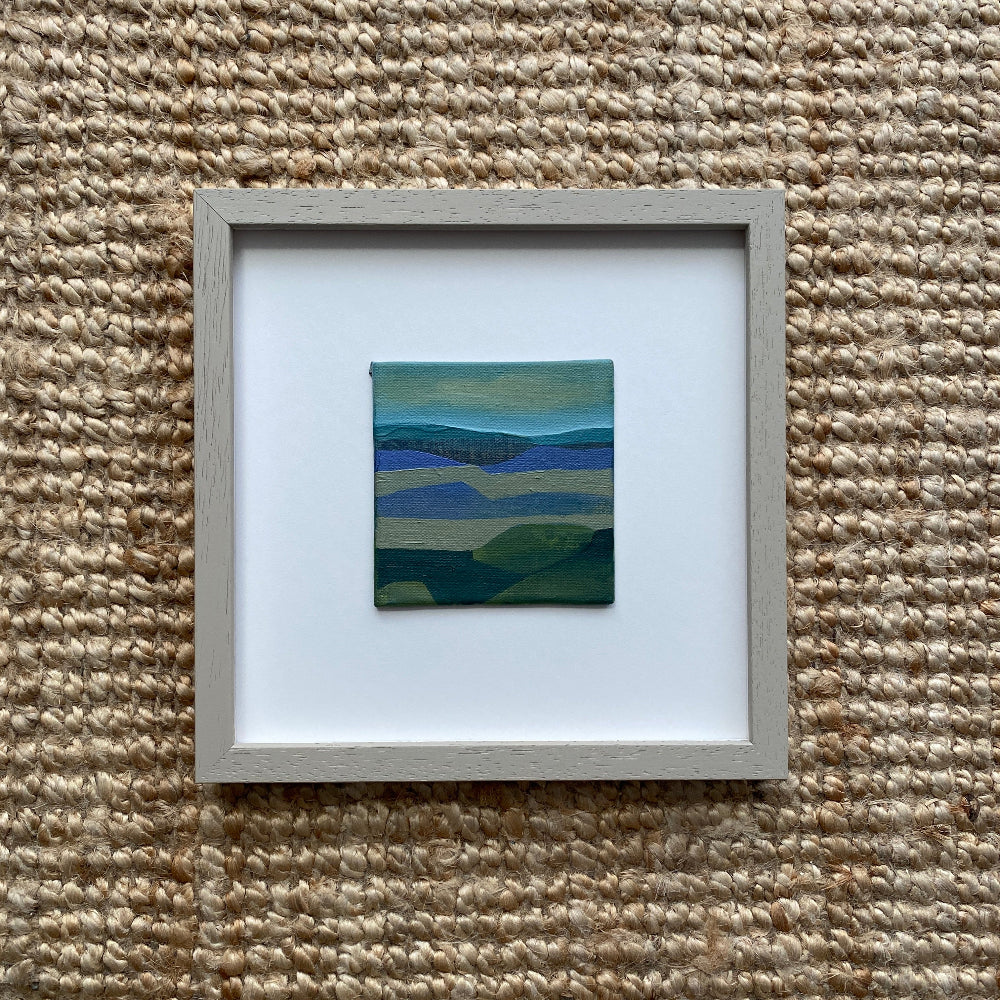 Framed artwork of an abstract landscape on a textured beige surface