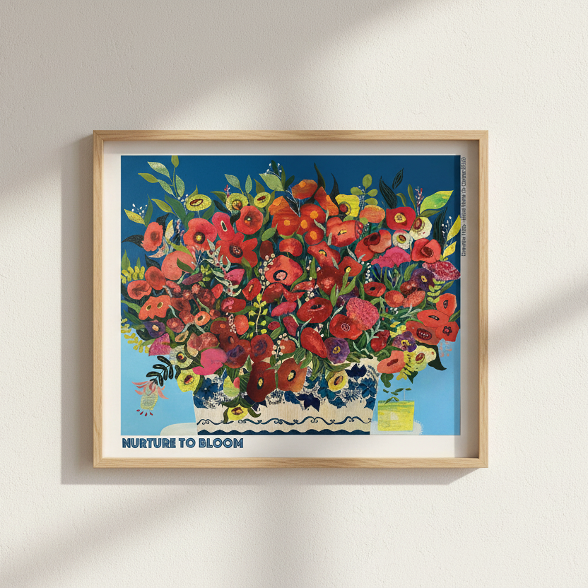 A framed art print featuring a colorful floral bouquet in a vase against a blue background, hung on a light beige wall with soft diagonal shadows. The print includes the text 'NURTURE TO BLOOM' at the bottom.