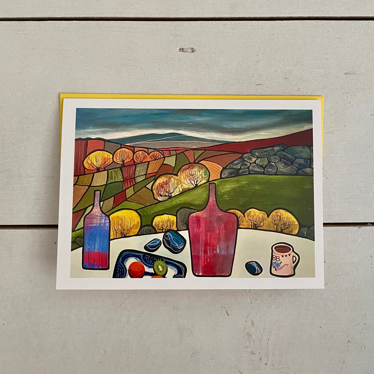 A square art print featuring a colorful still life landscape with two red bottles, a blue tray, and a small cup, displayed against a light gray wood plank background.