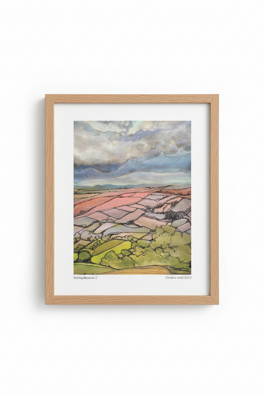 A framed watercolor landscape print featuring pink and green fields under a cloudy blue sky, presented in a light natural wood frame with a white mat against a white background.