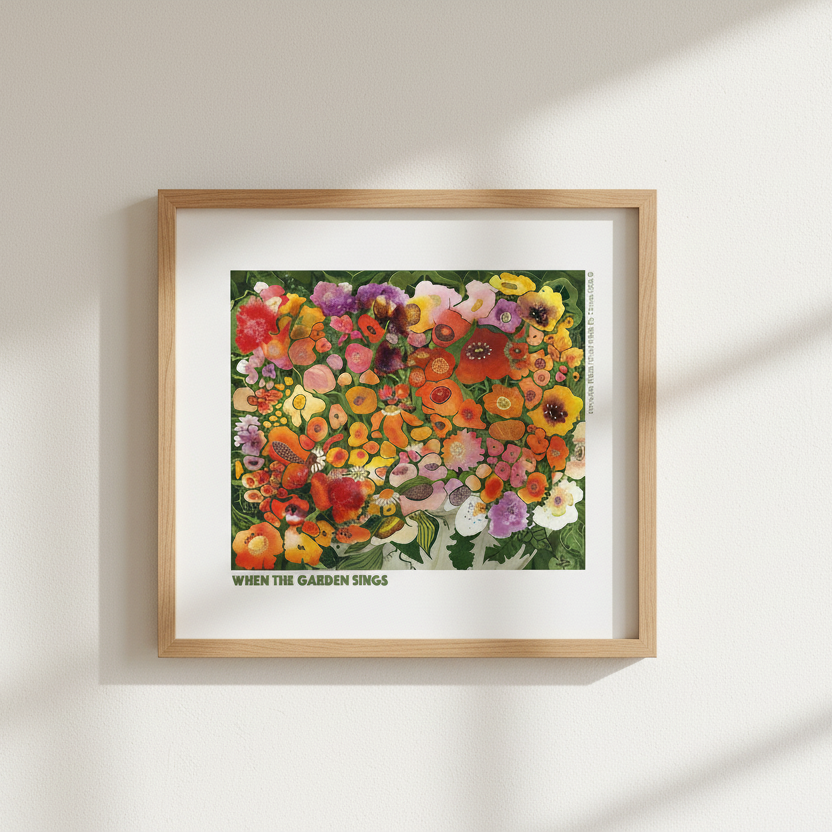 A framed art print featuring a colorful illustration of wildflowers with the text 'WHEN THE GARDEN BLOOMS' at the bottom, displayed on a clean white wall.